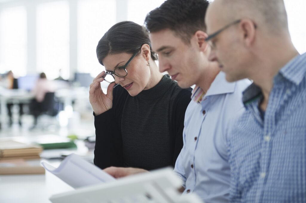 Three colleagues review documents together in a bright office.