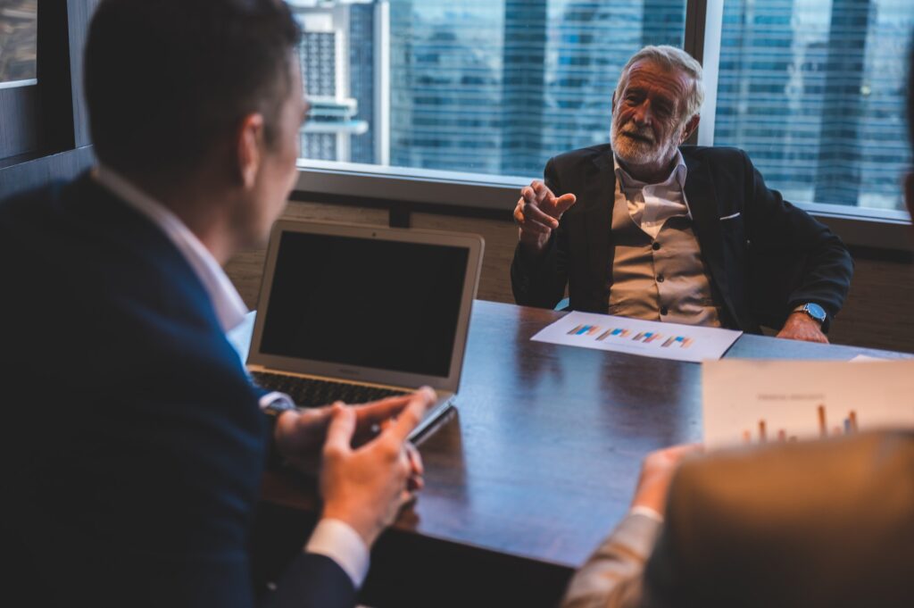 Business leaders discussing a decision across a conference table with reports and a laptop.