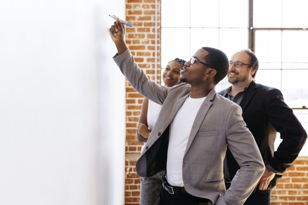 Three business colleagues discussing ideas at a whiteboard in a bright office.