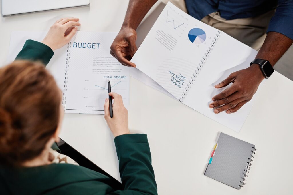 Two colleagues reviewing budget reports and charts at a desk.