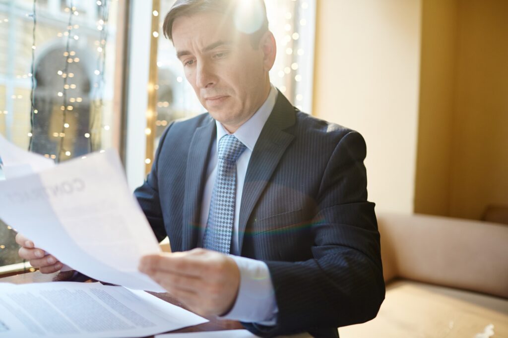 A business executive in a navy suit reviewing paper documents at a bright office table.
