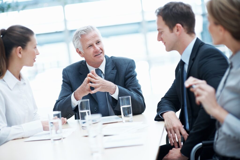 Four business colleagues discuss priorities around a conference table in a bright office.